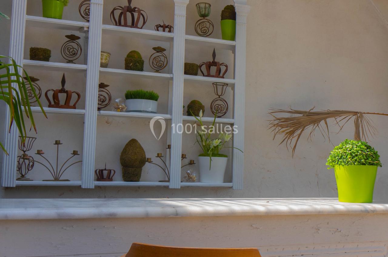 Étagère blanche décorative avec plantes et objets, devant un mur clair, une chaise en bois au premier plan.