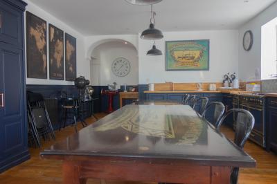 Salon avec fauteuils en cuir, table basse en bois, plante verte, bibliothèque et tableau sur un mur lambrissé.