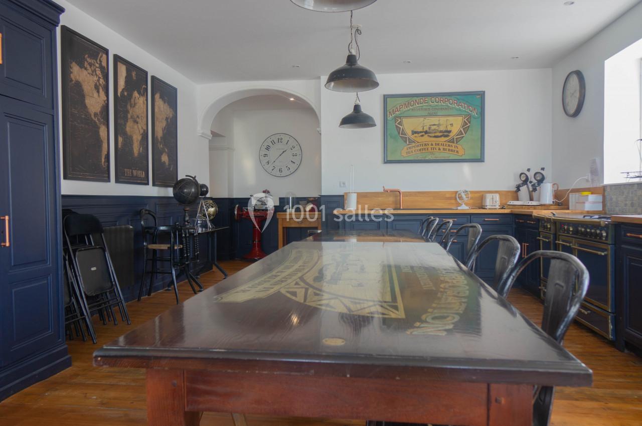Salle à manger avec une grande table en bois, chaises noires, meubles bleu foncé et décorations murales vintage.