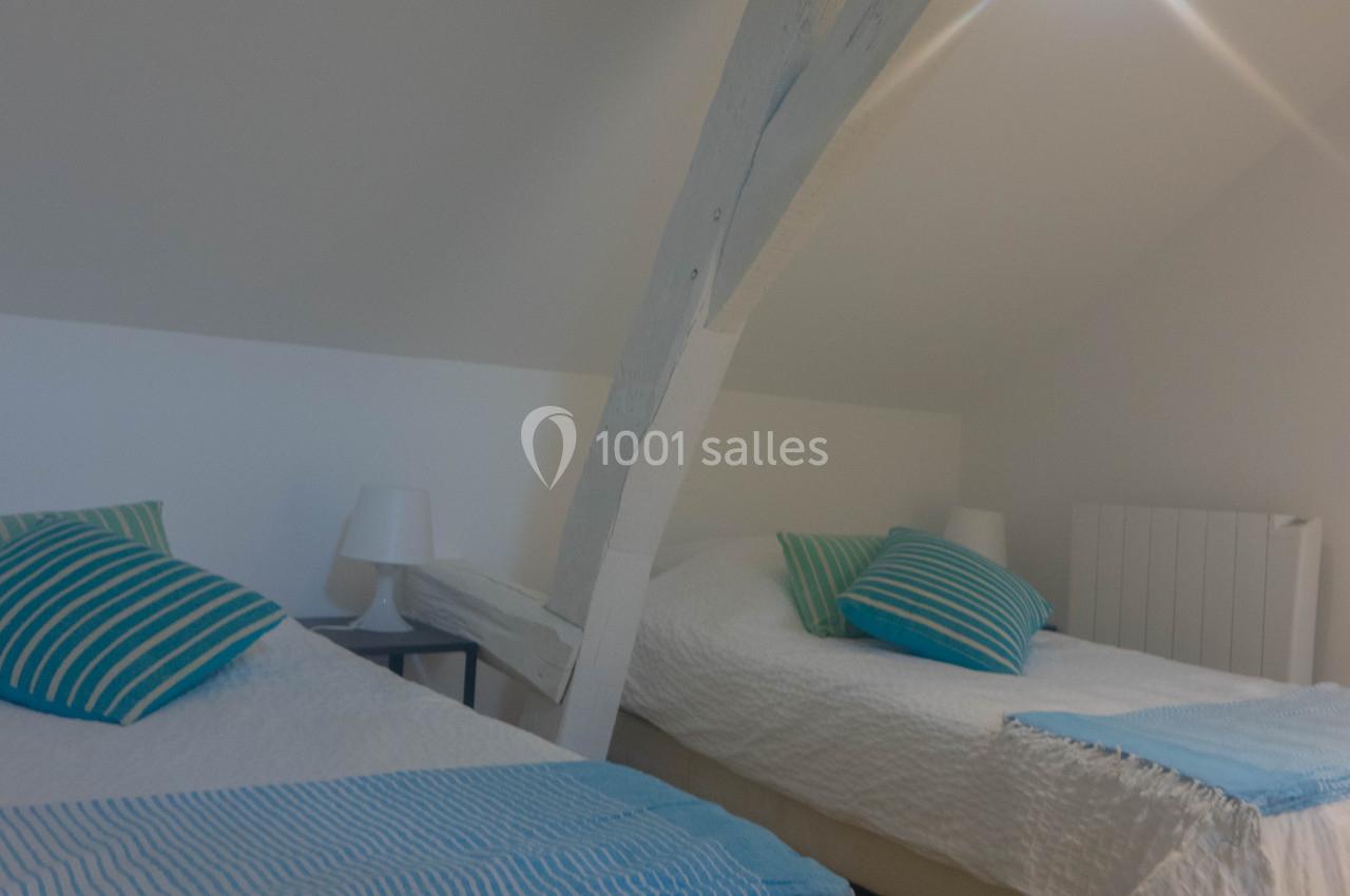 Deux lits simples avec draps blancs et coussins rayés bleus dans une chambre mansardée lumineuse.