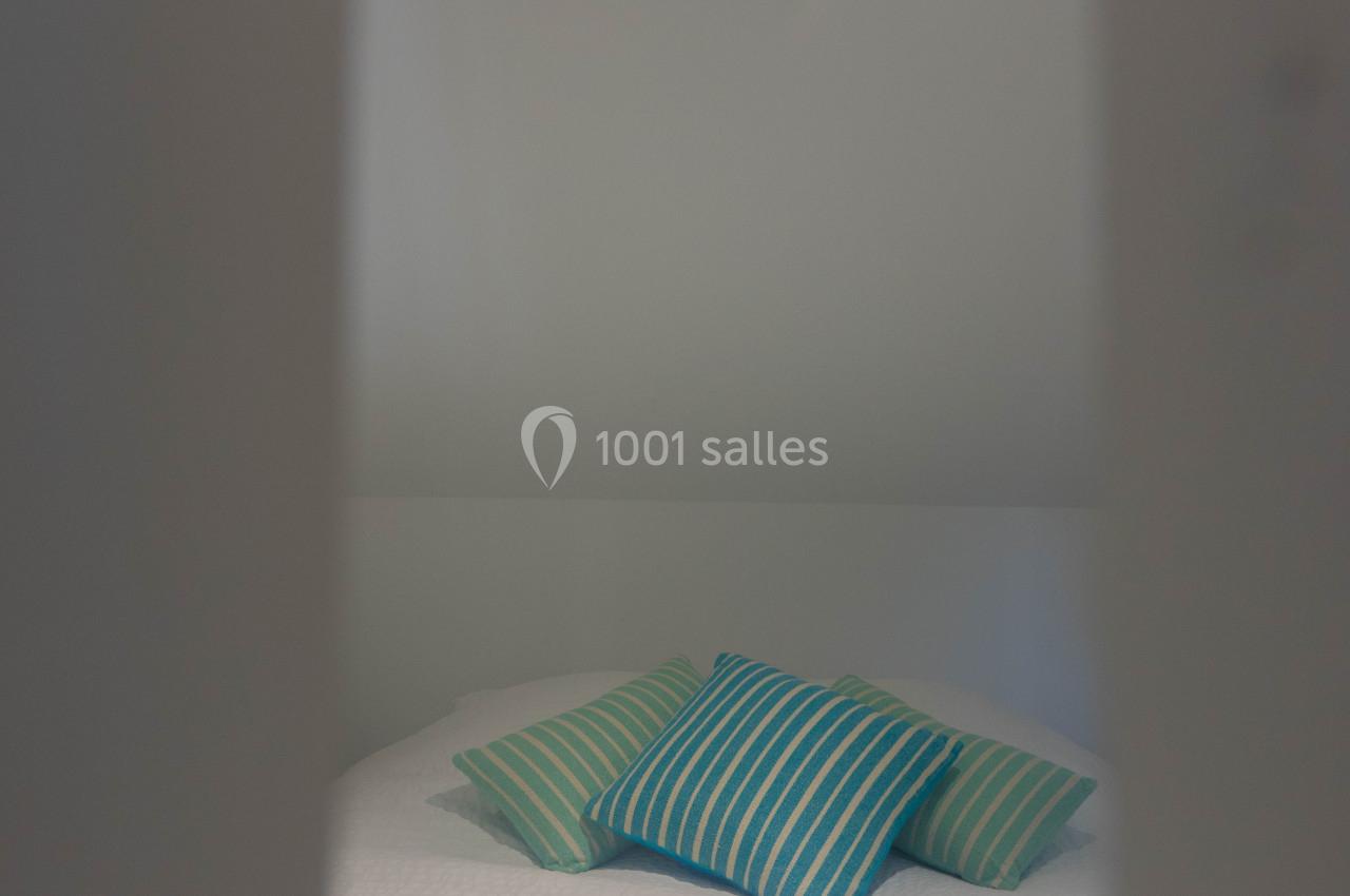 Lit avec une couverture bleue rayée et des coussins assortis, vu à travers une ouverture dans un espace lumineux.