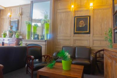 Salon avec fauteuils en cuir, table basse en bois, plante verte, bibliothèque et tableau sur un mur lambrissé.