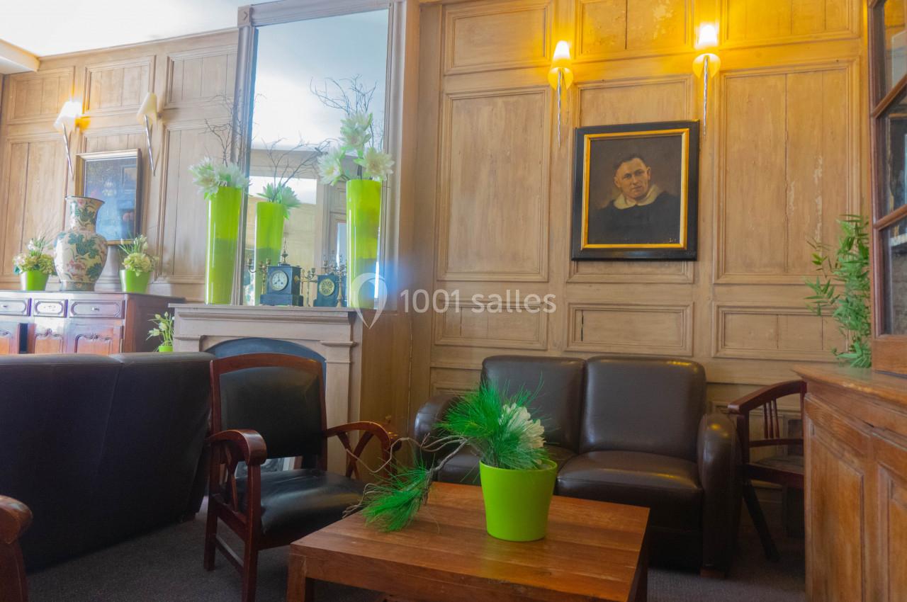 Salon avec fauteuils en cuir, table basse, plantes vertes en pots et portrait encadré sur un mur en bois clair.