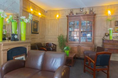 Salon avec fauteuils en cuir, table basse en bois, plante verte, bibliothèque et tableau sur un mur lambrissé.