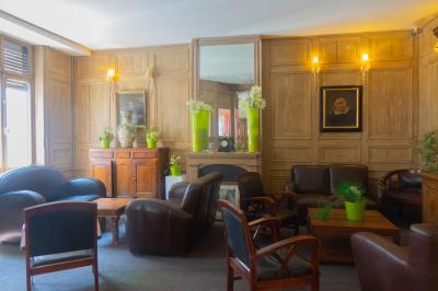 Salon avec fauteuils en cuir, table basse en bois, plante verte, bibliothèque et tableau sur un mur lambrissé.
