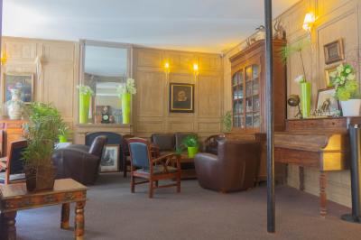 Salon avec fauteuils en cuir, table basse en bois, plante verte, bibliothèque et tableau sur un mur lambrissé.