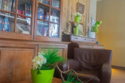 Salon avec fauteuils en cuir, table basse en bois, plante verte, bibliothèque et tableau sur un mur lambrissé.