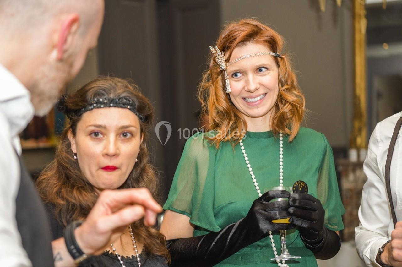 Deux femmes et un homme discutent lors d'un événement, vêtus de tenues élégantes d'inspiration rétro.