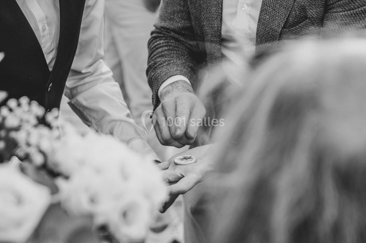 Deux hommes en tenue formelle observent un objet rond tenu dans la main de l'un d'eux, entourés de fleurs.
