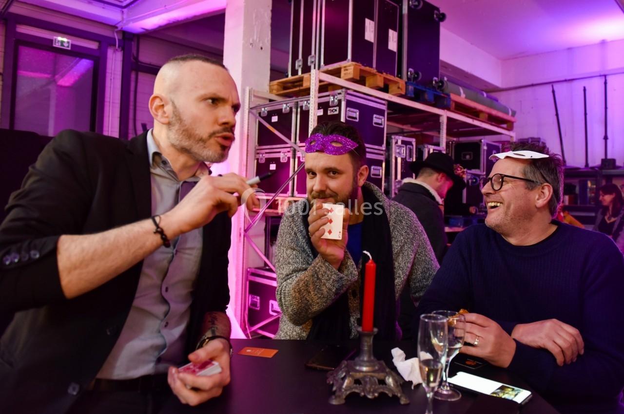 Trois hommes discutent autour d'une table avec des cartes, dans une ambiance festive et éclairage coloré.