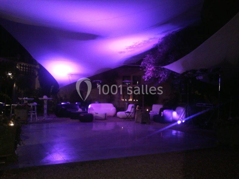 Espace extérieur éclairé par des lumières violettes, avec des sièges, des tables et une ambiance nocturne.