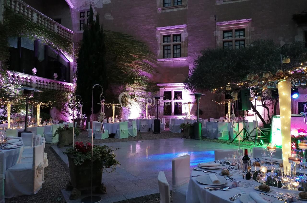 Cour intérieure éclairée pour un dîner en plein air, avec tables dressées, décorations lumineuses et ambiance festive.