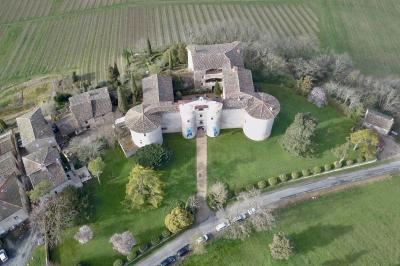 Vue aérienne d'un bâtiment historique entouré de jardins, de vignes et de maisons dans un paysage rural.