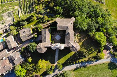 Vue aérienne d'un bâtiment historique entouré de jardins, de vignes et de maisons dans un paysage rural.