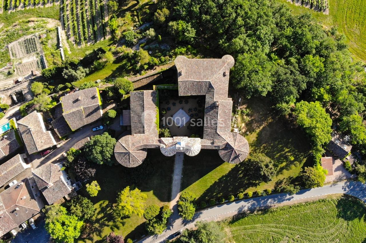 Vue aérienne d'un bâtiment historique entouré de jardins, de vignes et de maisons dans un paysage rural.