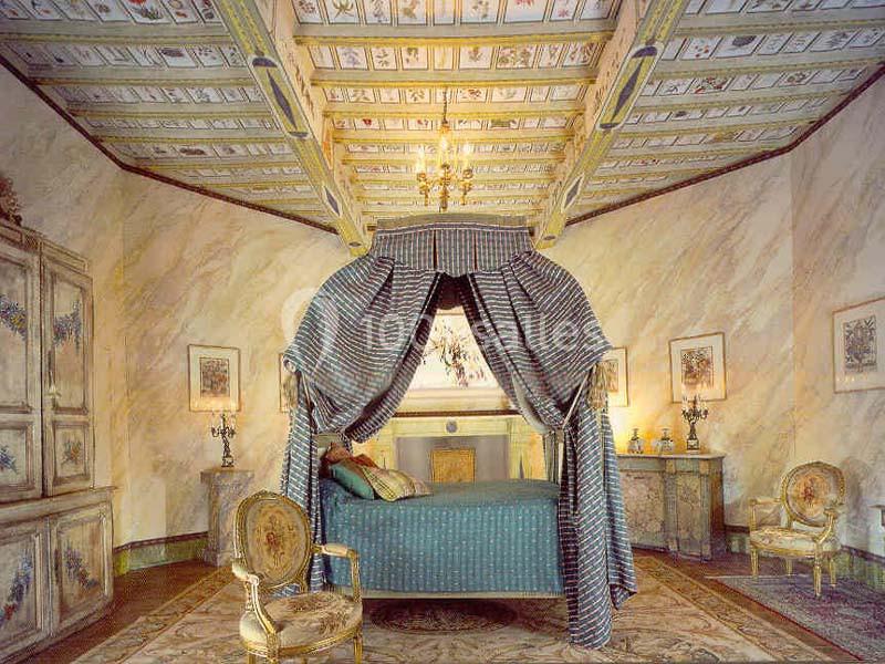 Chambre élégante avec lit à baldaquin, plafond décoré, meubles anciens et éclairage chaleureux.