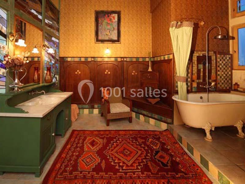 Salle de bain rétro avec baignoire sur pieds, meubles en bois, tapis coloré et éclairage chaleureux.
