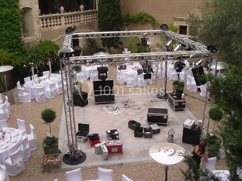 Installation d'équipements audiovisuels sous une structure métallique dans une cour aménagée pour un événement.