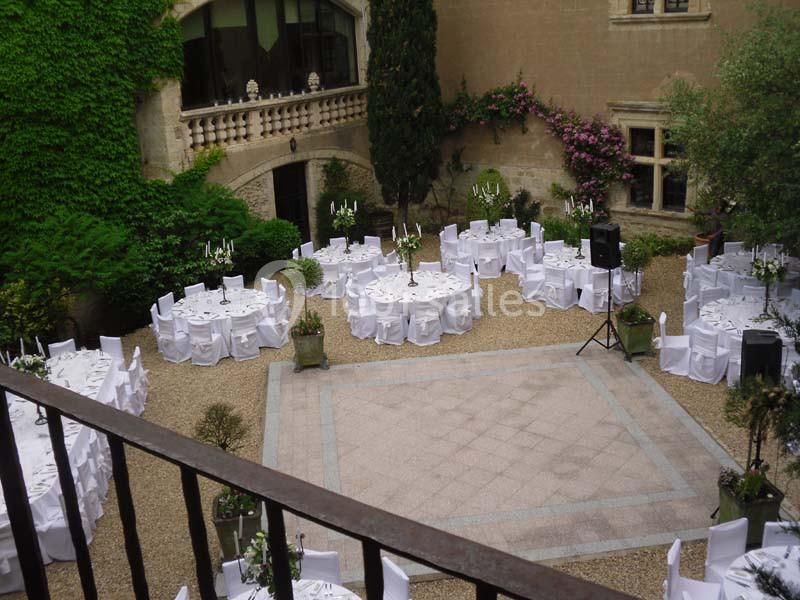 Cour intérieure aménagée pour un événement, avec des tables rondes dressées et des chaises blanches disposées en cercle.
