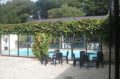 Piscine intérieure visible à travers une baie vitrée entourée de murs recouverts de plantes grimpantes, avec des tables…