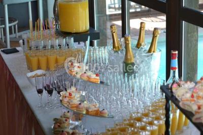 Piscine intérieure visible à travers une baie vitrée entourée de murs recouverts de plantes grimpantes, avec des tables…