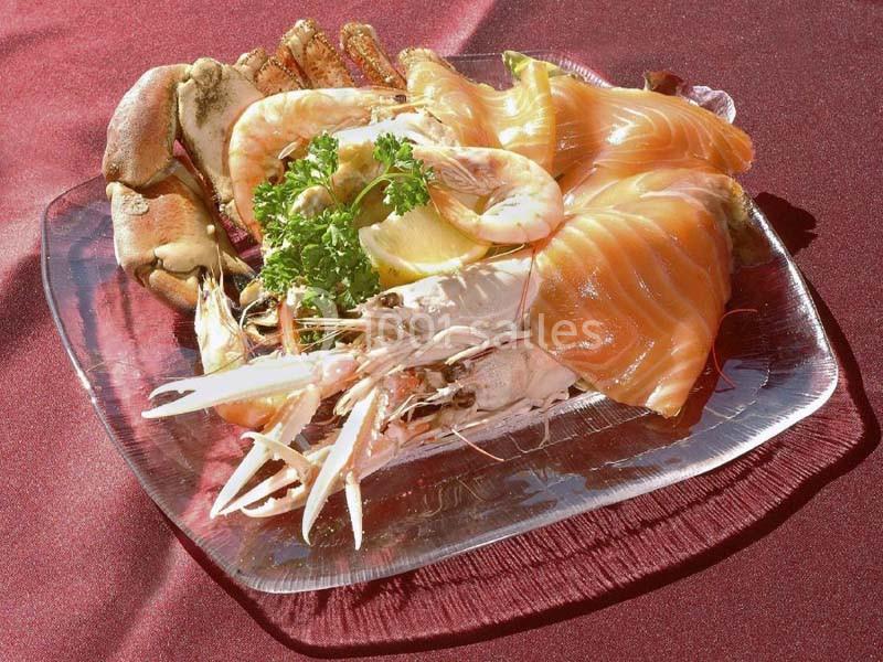 Assiette de fruits de mer avec crevettes, saumon fumé, crabe, citron et persil sur une nappe rouge.