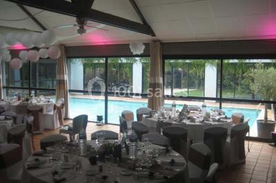 Piscine intérieure visible à travers une baie vitrée entourée de murs recouverts de plantes grimpantes, avec des tables…