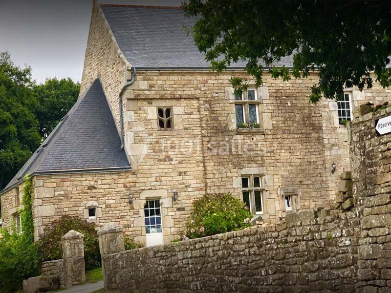 Maison en pierre traditionnelle avec toit en ardoise, entourée d'un muret en pierre et de végétation.