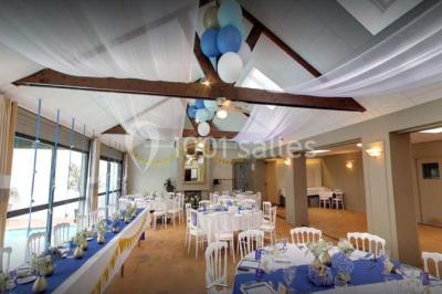 Piscine intérieure visible à travers une baie vitrée entourée de murs recouverts de plantes grimpantes, avec des tables…