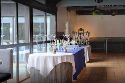 Piscine intérieure visible à travers une baie vitrée entourée de murs recouverts de plantes grimpantes, avec des tables…