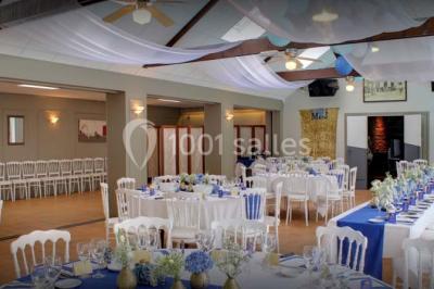Piscine intérieure visible à travers une baie vitrée entourée de murs recouverts de plantes grimpantes, avec des tables…
