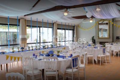 Piscine intérieure visible à travers une baie vitrée entourée de murs recouverts de plantes grimpantes, avec des tables…