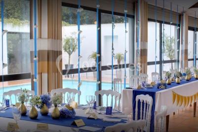 Piscine intérieure visible à travers une baie vitrée entourée de murs recouverts de plantes grimpantes, avec des tables…