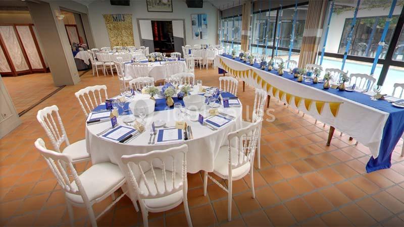 Salle de réception décorée avec des tables rondes et une longue table, nappes blanches et accents bleus.
