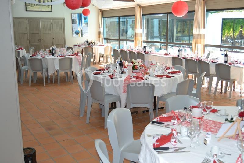 Salle décorée pour un événement avec des tables rondes dressées, nappes blanches et touches de rouge.