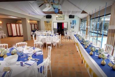 Piscine intérieure visible à travers une baie vitrée entourée de murs recouverts de plantes grimpantes, avec des tables…