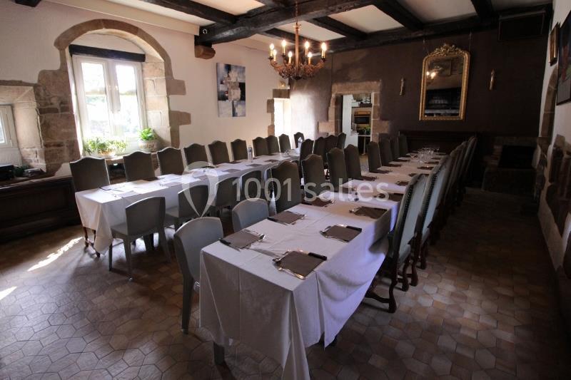 Salle de réception avec longues tables dressées, nappes blanches, chaises alignées et lumière naturelle entrant par une…