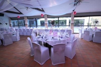 Piscine intérieure visible à travers une baie vitrée entourée de murs recouverts de plantes grimpantes, avec des tables…