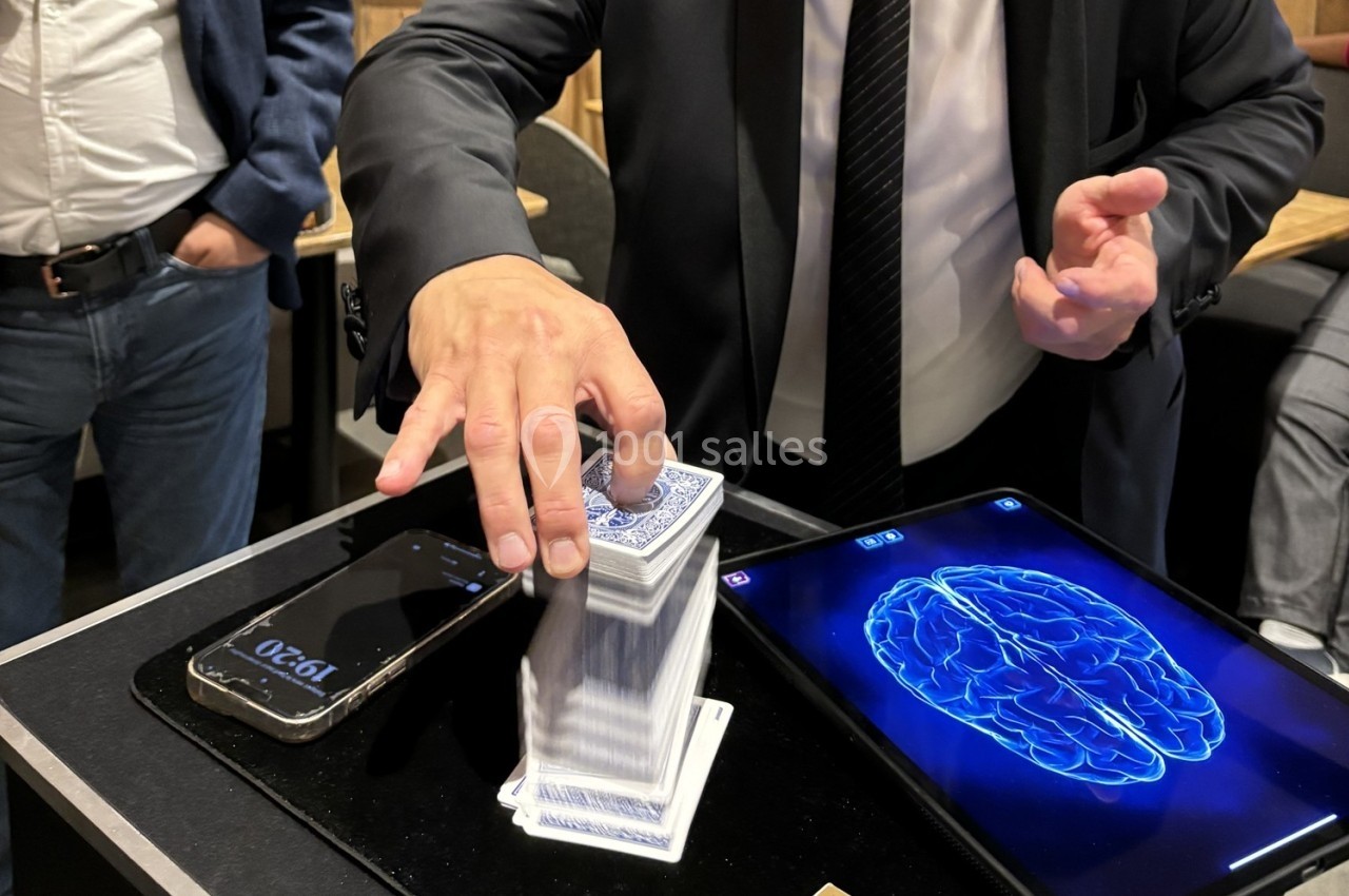 Un homme en costume manipule un jeu de cartes sur une table avec un smartphone et une tablette affichant un cerveau.