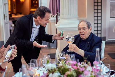 Un homme en costume verse une boisson depuis une tablette numérique dans un verre, illustrant un effet magique.