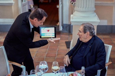 Un homme en costume verse une boisson depuis une tablette numérique dans un verre, illustrant un effet magique.