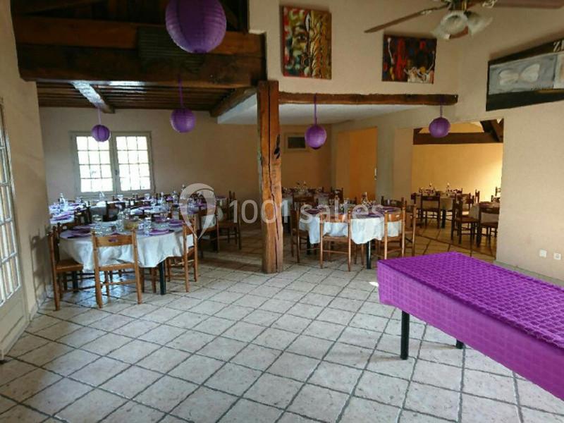 Salle de réception décorée avec des tables dressées, des nappes blanches et des lanternes violettes suspendues.
