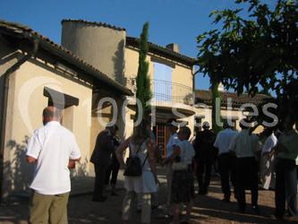 Un groupe de personnes discutant devant une maison ensoleillée avec des arbres et des volets fermés.
