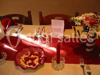 Table dressée avec une nappe beige, chemin de table rouge, vaisselle, bougie rouge et bouquet de fleurs colorées.