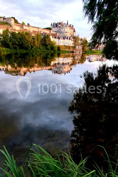 Reflet d'un château et de ses remparts dans une rivière calme, entouré de verdure et d'arbres au crépuscule.