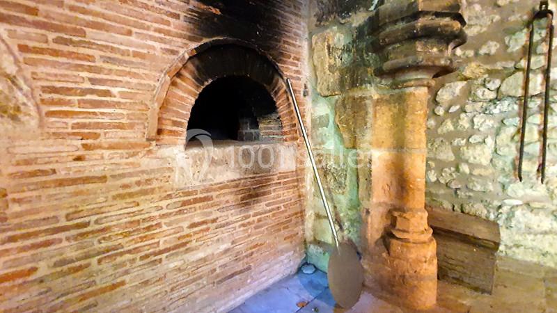 Four à pain ancien en briques et pierres, avec une pelle en métal appuyée contre le mur.