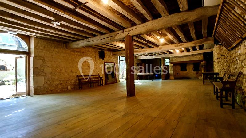 Salle intérieure spacieuse avec poutres en bois apparentes, murs en pierre et mobilier rustique.