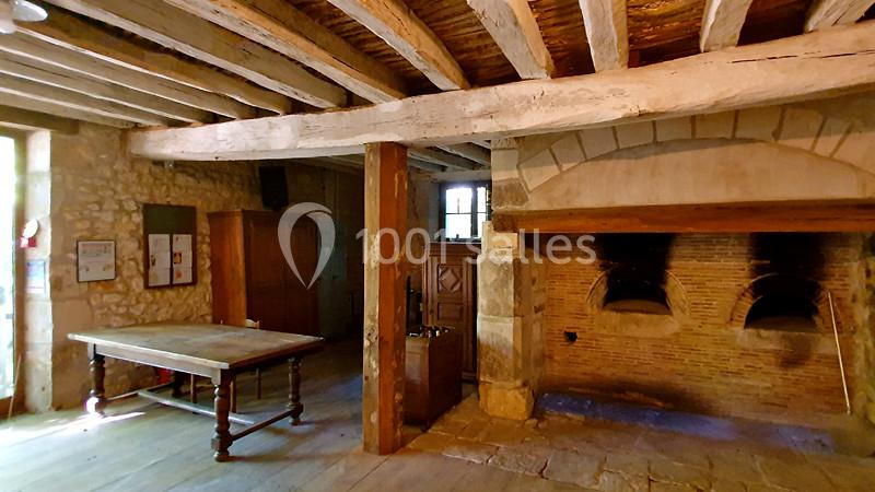 Intérieur d'une ancienne boulangerie avec un four en pierre, une table en bois et des murs en pierre apparente.