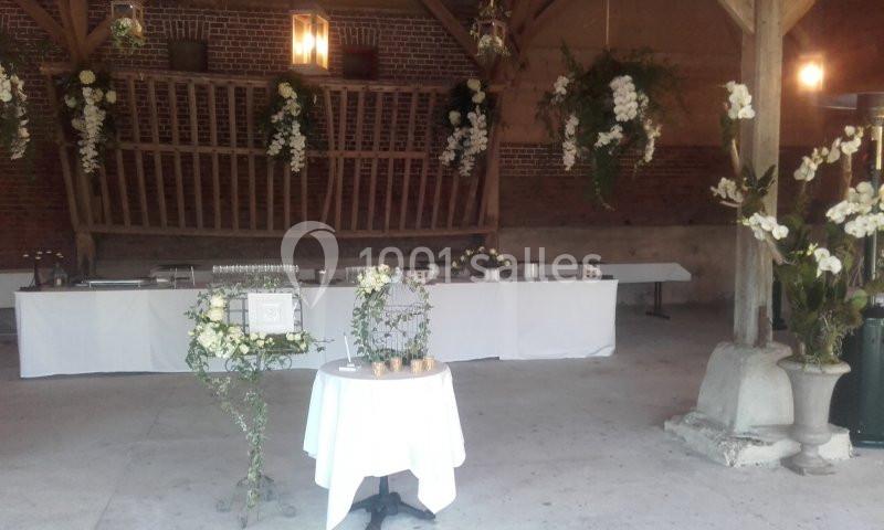 Salle de réception décorée avec des fleurs blanches suspendues et une table ronde ornée de bougies.