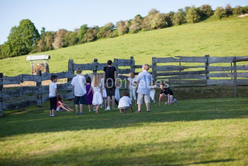Des enfants jouent en groupe sur une pelouse près d'une clôture en bois, dans un paysage de campagne verdoyant.